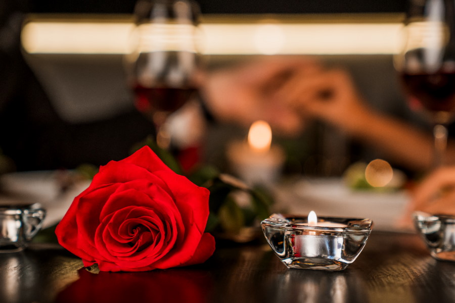 Romantic dinner date at night with focus on red rose and candles on the foreground